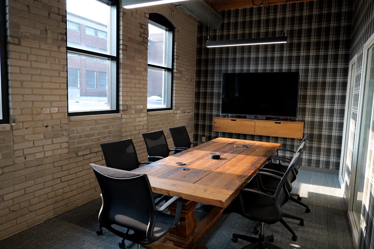 Boom Island meeting room: reclaimed-wood table, black chairs, exposed brick and plaid wallcovering