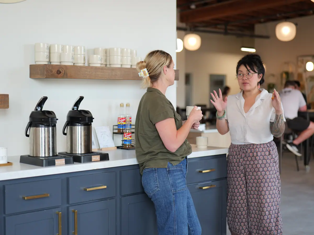 Two women talking at a coffee bar with navy cabinets and brass pulls