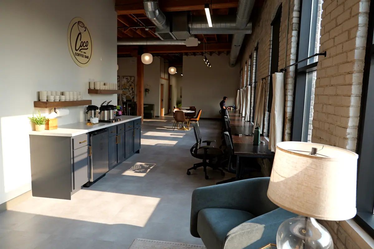 Long coffee bar and lounge running beside tall arched windows, a table lamp in the foreground