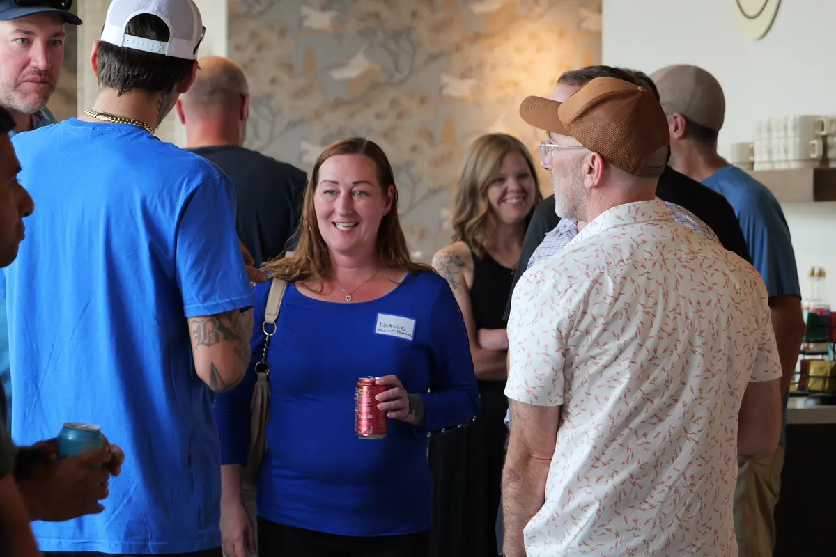 A smiling guest in a blue top talks with others at a crowded reception