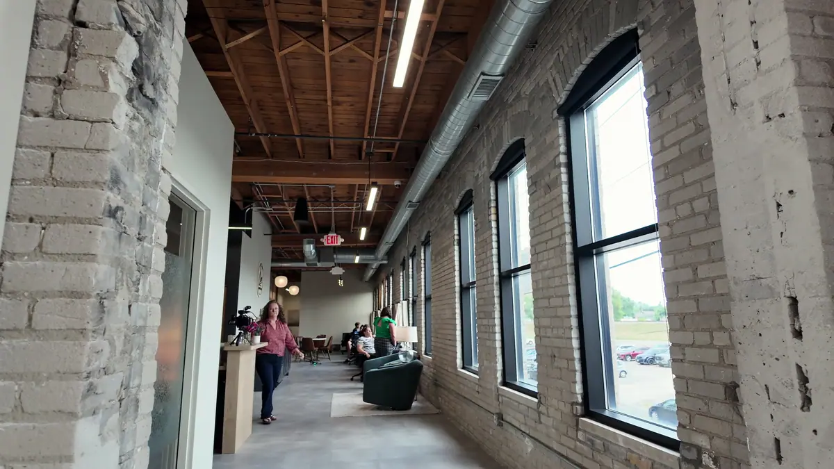 A long brick-and-timber coworking corridor with tall arched windows, a member walking toward camera