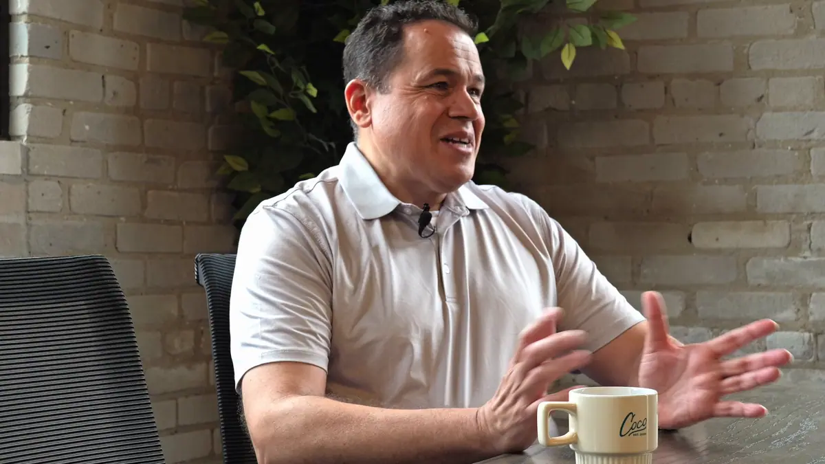 Side camera angle of a member speaking at a table during a filmed interview