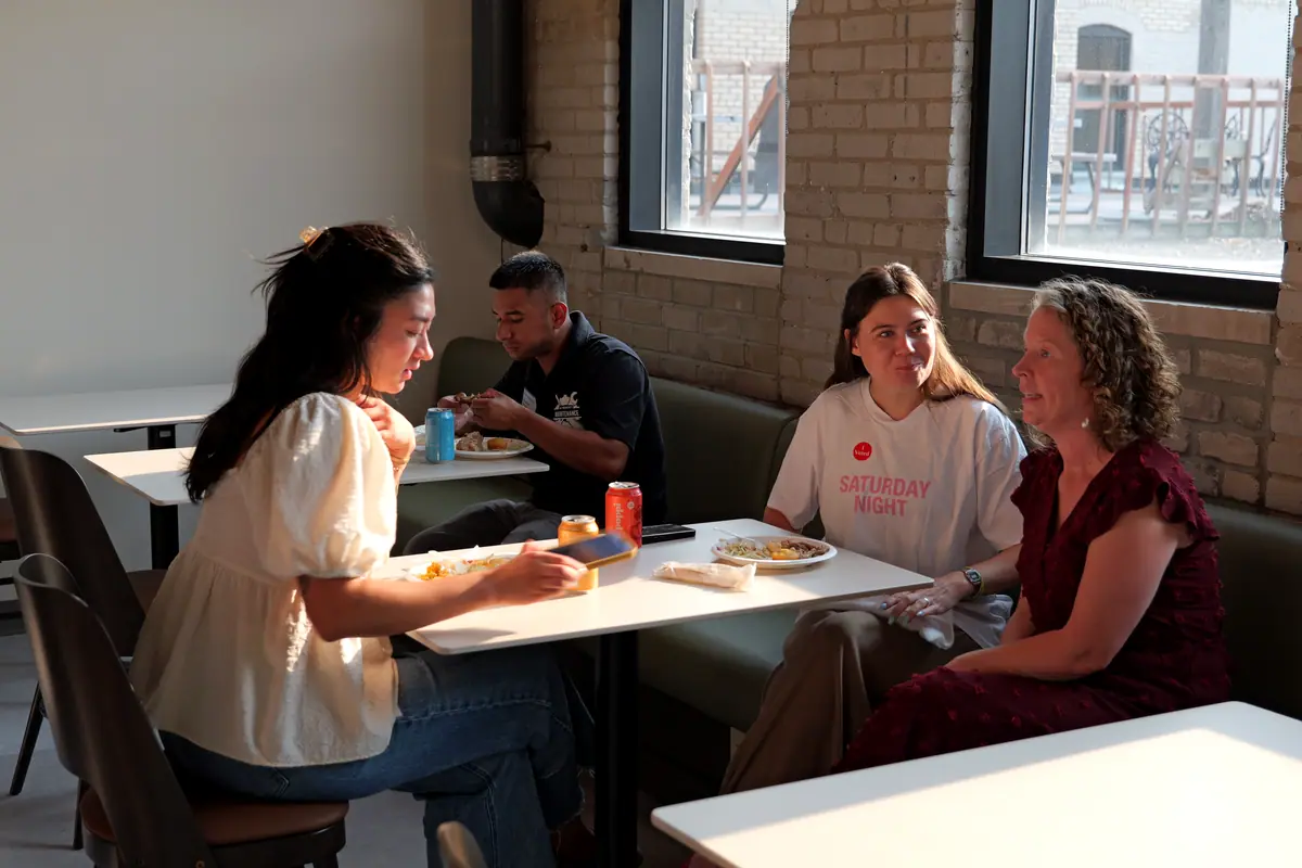 Members share lunch at small tables in a window-lit lounge