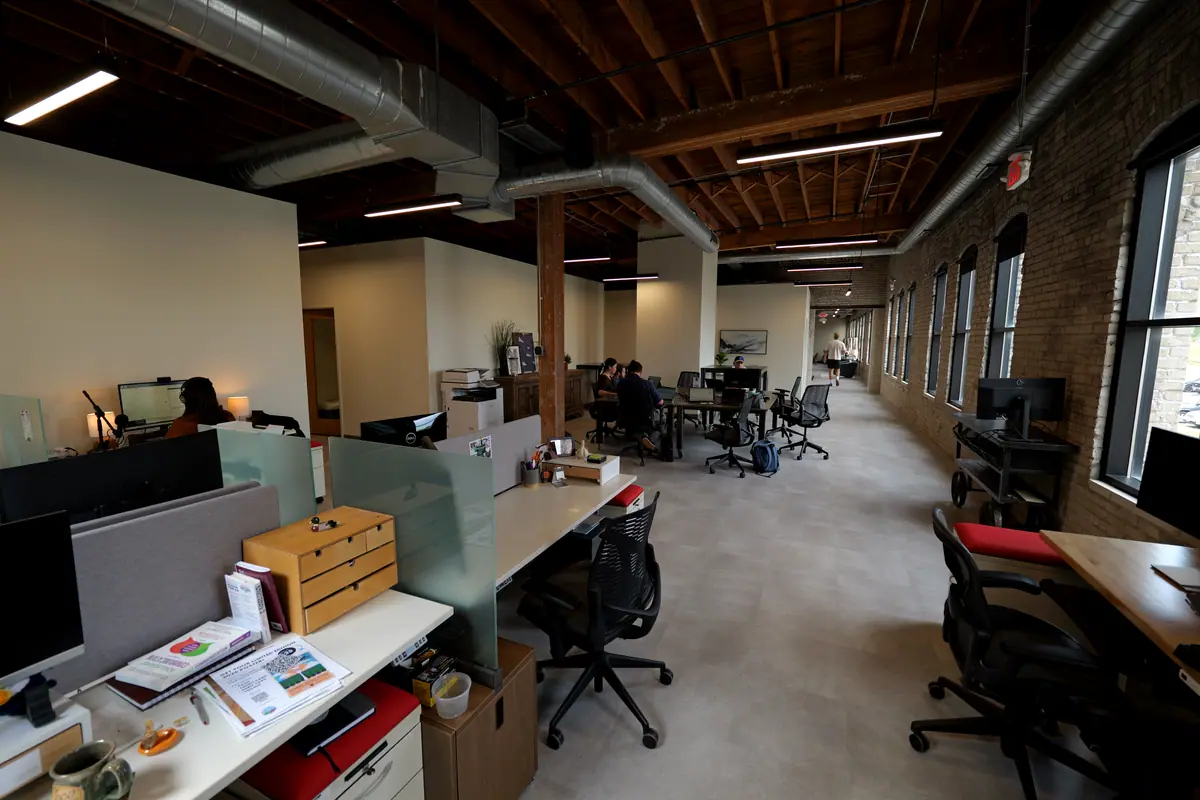 Open coworking floor with dedicated desks under a timber ceiling and industrial ductwork
