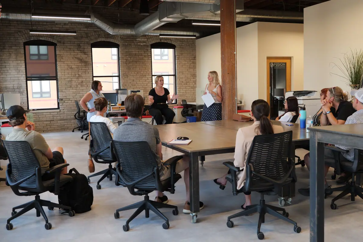 A team meeting around long tables in a sunlit brick loft